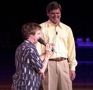 Dana Carvey holds a microphone on stage with AOL founder Steve Case.