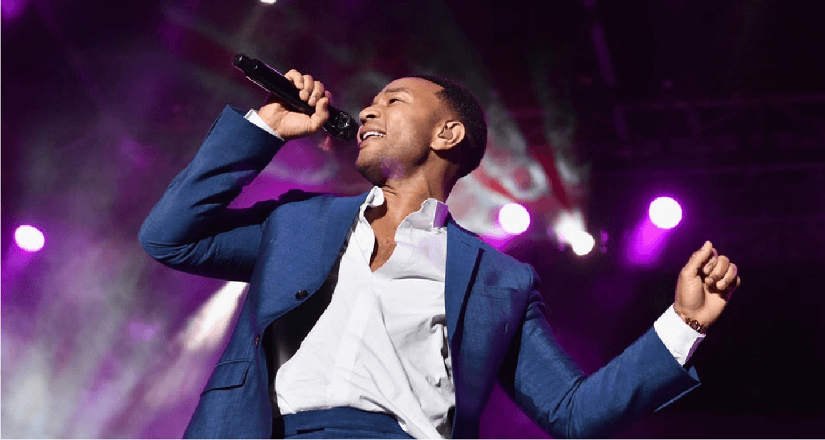 John Legend singing into a microphone on stage.